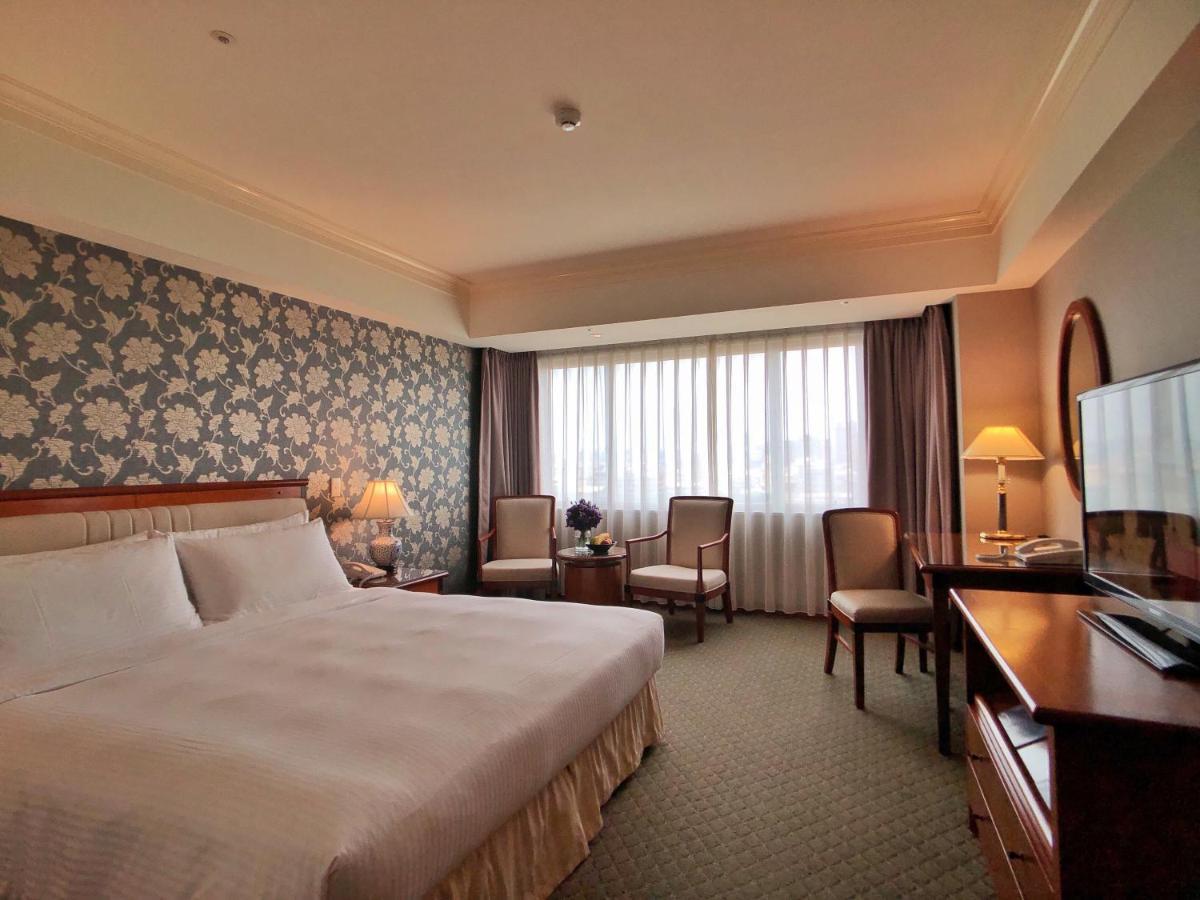 Evergreen Laurel Hotel - Taichung Bagian luar foto The photo shows a well-appointed hotel room. It features a large bed with white bedding and a decorative headboard. The walls are adorned with a patterned wallpaper, possibly floral, adding a touch of elegance. There is a window with sheer curtains t