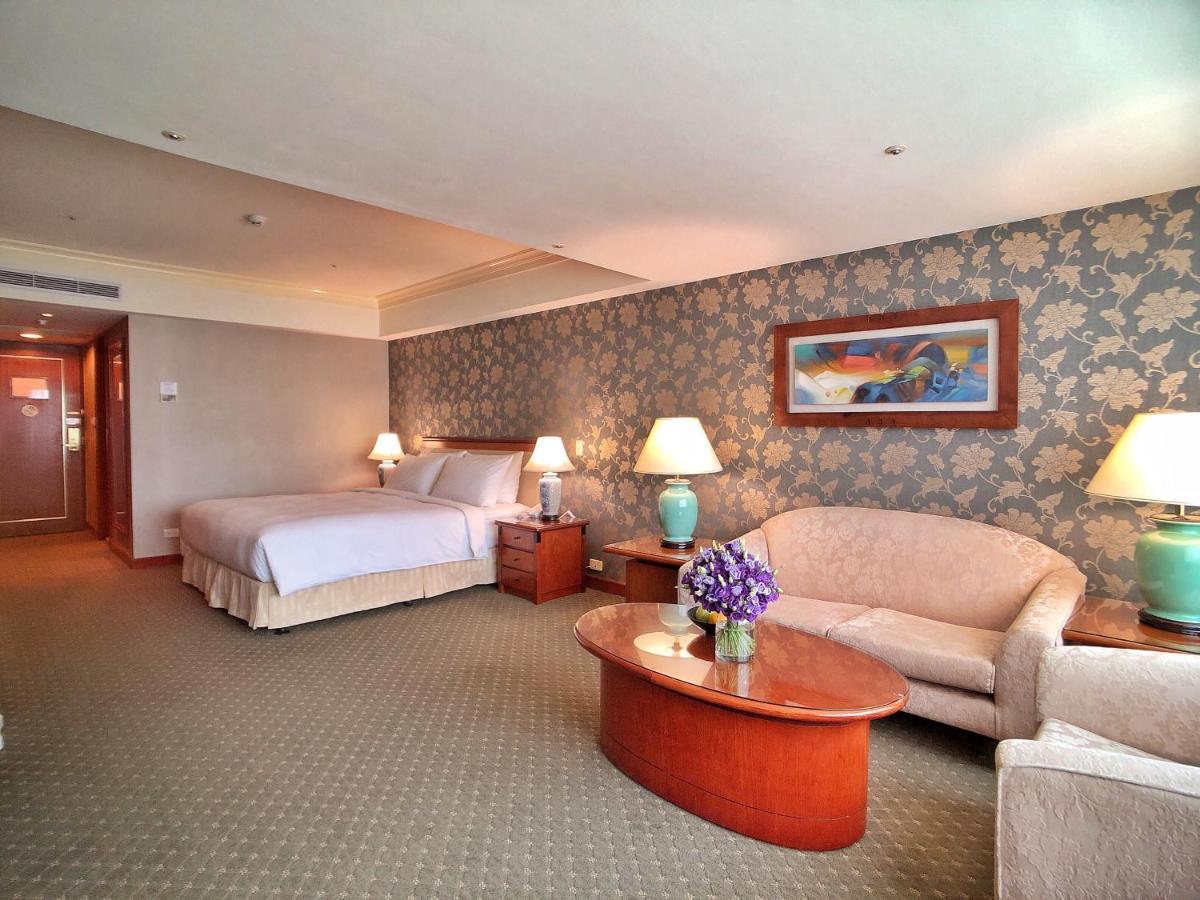 Evergreen Laurel Hotel - Taichung Bagian luar foto The photo shows a hotel room that features a well-furnished space. It includes a large bed with a light-colored bedspread, a comfortable sofa, and armchair. There's a coffee table with a vase of flowers in the center. The room has a decorative wallpa
