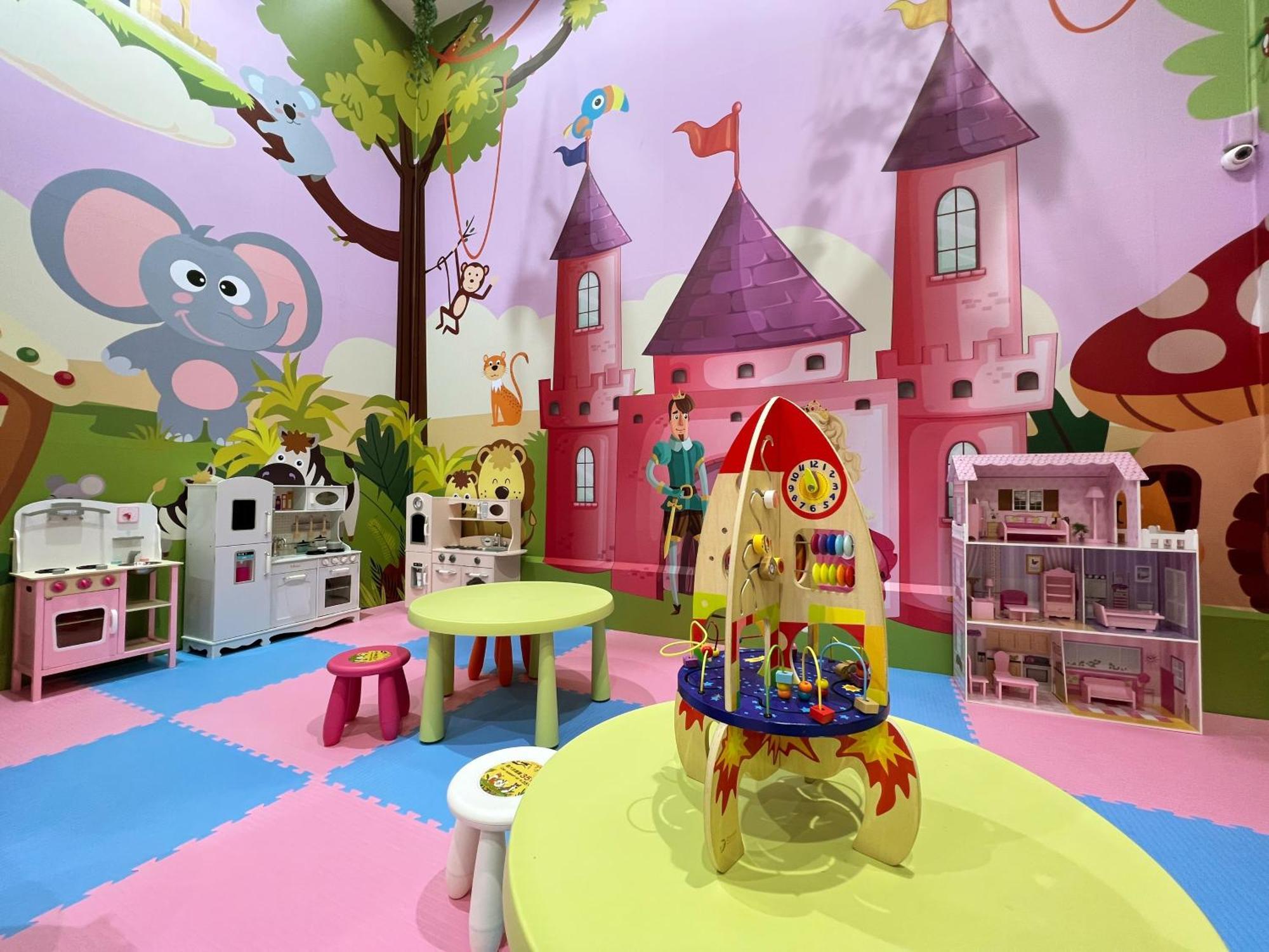 Evergreen Laurel Hotel - Taichung Bagian luar foto The photo shows a colorful children's playroom designed with a whimsical theme. The walls are painted in bright colors and feature a cartoon-style mural of a pink castle with purple towers and a smiling cartoon elephant. The room is filled with playf