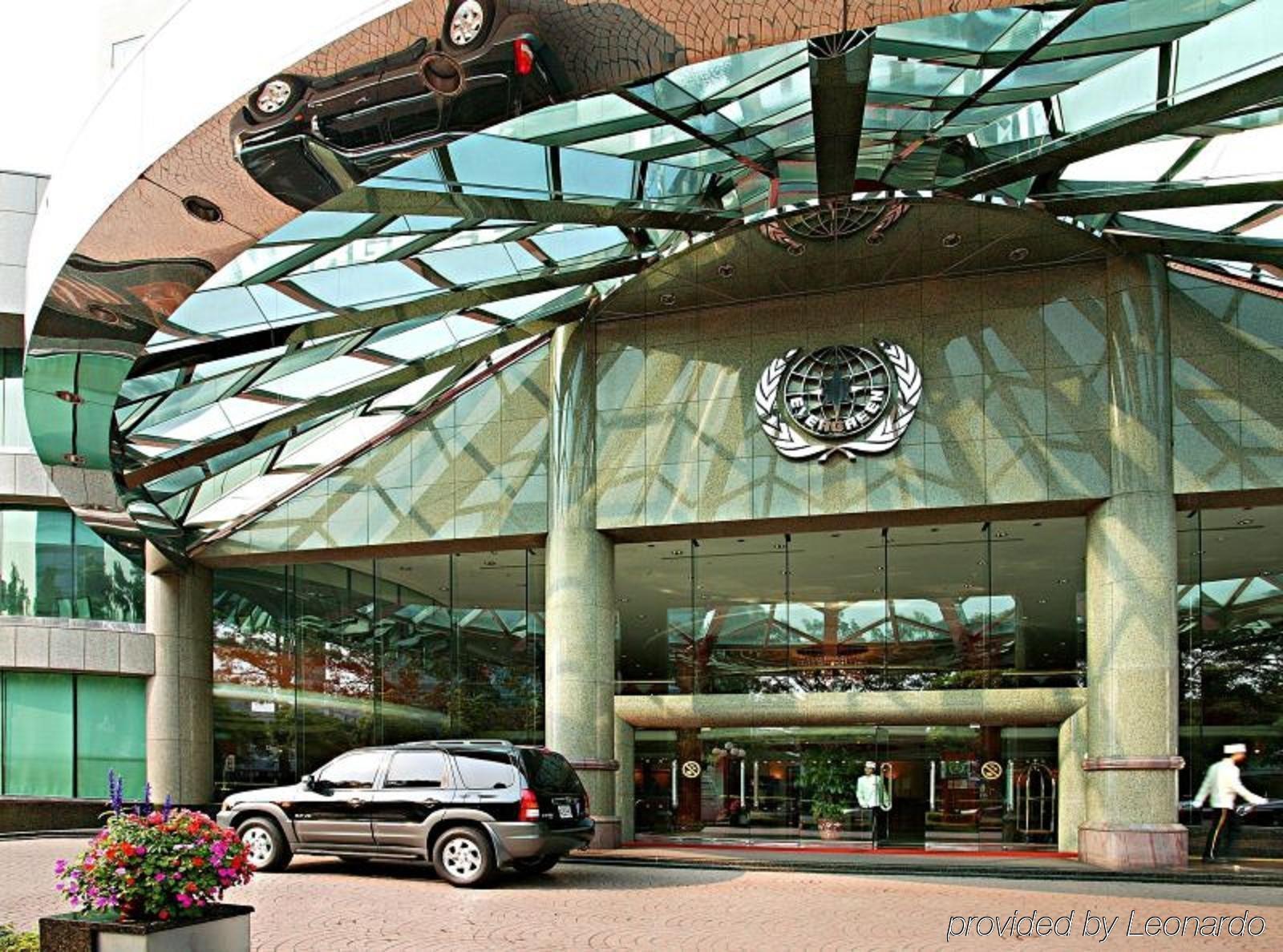 Evergreen Laurel Hotel - Taichung Bagian luar foto The photo shows the entrance of a modern building characterized by its glass and metal architecture. The structure features a large, domed roof that reflects light, with a distinctive emblem or logo displayed prominently at the center. In front of th