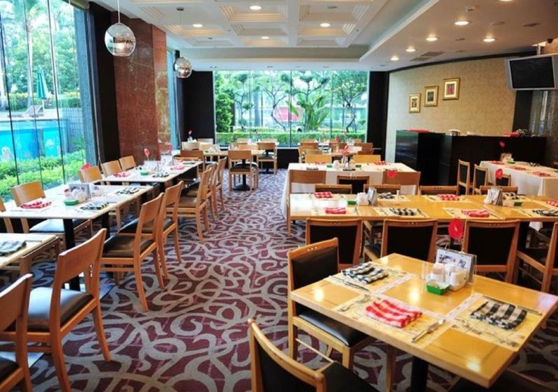 Evergreen Laurel Hotel - Taichung Bagian luar foto The photo shows an interior of a restaurant with a spacious layout. There are several wooden tables, each set with napkins and utensils. The floor has a decorative carpet, and large windows provide a view of greenery outside. The lighting is bright, 
