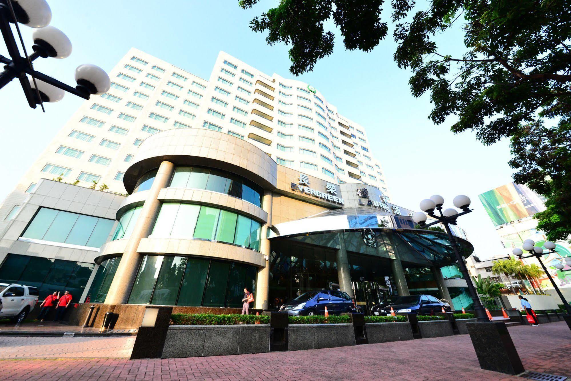 Evergreen Laurel Hotel - Taichung Bagian luar foto The photo shows a modern multi-story building, which appears to be a hotel or commercial establishment. The structure has a rounded glass entrance with a distinctive architectural design, featuring large windows. The building is surrounded by greener