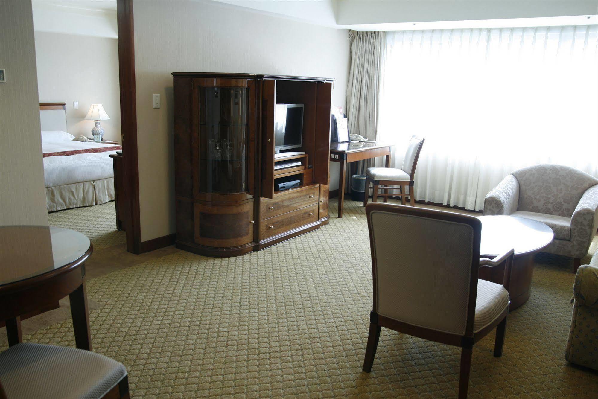 Evergreen Laurel Hotel - Taichung Bagian luar foto The photo shows an interior of a hotel room suite. The space includes a living area with several pieces of furniture. There is a coffee table and chairs, creating a comfortable seating area. A wooden cabinet with a TV inside is situated against one w