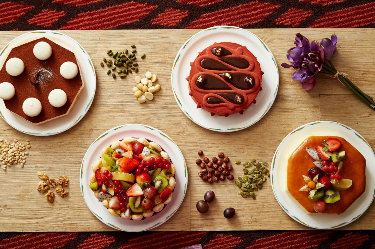 Evergreen Laurel Hotel - Taichung Bagian luar foto The photo displays a variety of desserts arranged on small plates. There are three main cakes or tarts:

1. **Top Left Plate**: A round chocolate cake with a smooth surface and white decorations on top.
2. **Top Middle Plate**: Another cake, possibly