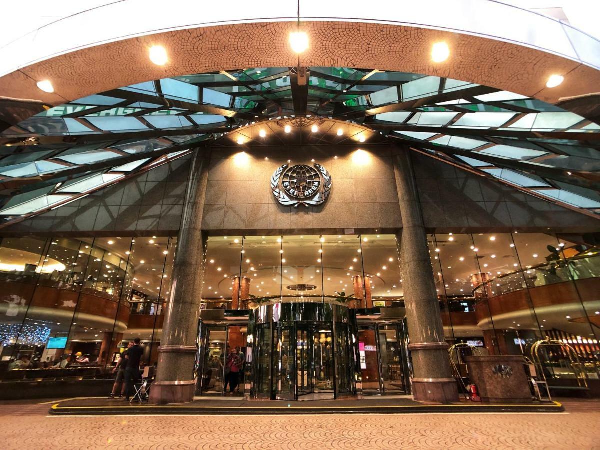 Evergreen Laurel Hotel - Taichung Bagian luar foto The image shows the entrance of a modern building, likely a hotel or a luxury establishment. The entrance features a large revolving door surrounded by glass panels. Above the entrance, there is a prominent logo or emblem. The overall architectural d