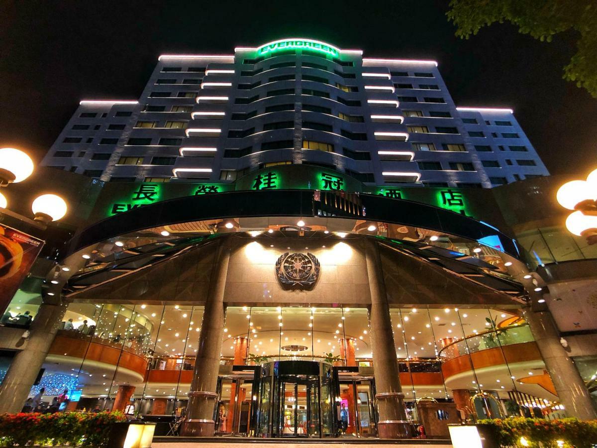 Evergreen Laurel Hotel - Taichung Bagian luar foto The photo shows a modern building at night, featuring a grand entrance with illuminated signage. The structure has multiple stories with a sleek design, adorned with green lighting that highlights its architectural features. The entrance is spacious 