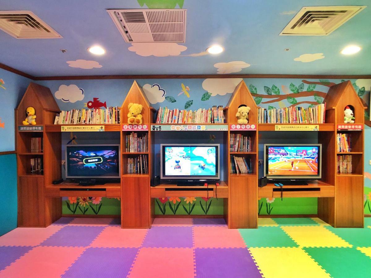 Evergreen Laurel Hotel - Taichung Bagian luar foto The photo shows a colorful and playful room designed for children. In the center, there are three wooden gaming stations, each equipped with a television screen and surrounded by shelves filled with books. The walls are decorated with cheerful images