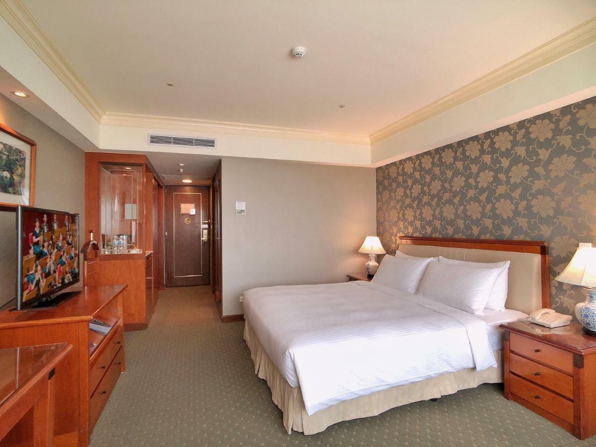 Evergreen Laurel Hotel - Taichung Bagian luar foto The photo shows a well-furnished hotel room. It features a large bed with white linens positioned against a decorative wall. On either side of the bed are bedside tables with lamps. There’s a television mounted on a wooden cabinet across from the bed