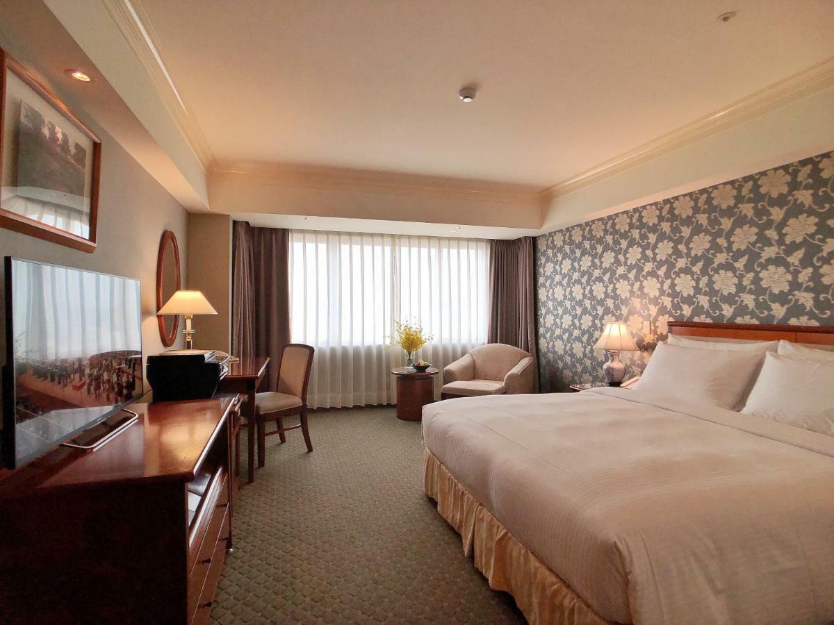 Evergreen Laurel Hotel - Taichung Bagian luar foto The photo shows a hotel room with a spacious layout. It features a large bed with white bedding, bedside lamps, and a decorative headboard. There is a comfortable seating area with an armchair and small table. A desk is present, complete with a lamp 