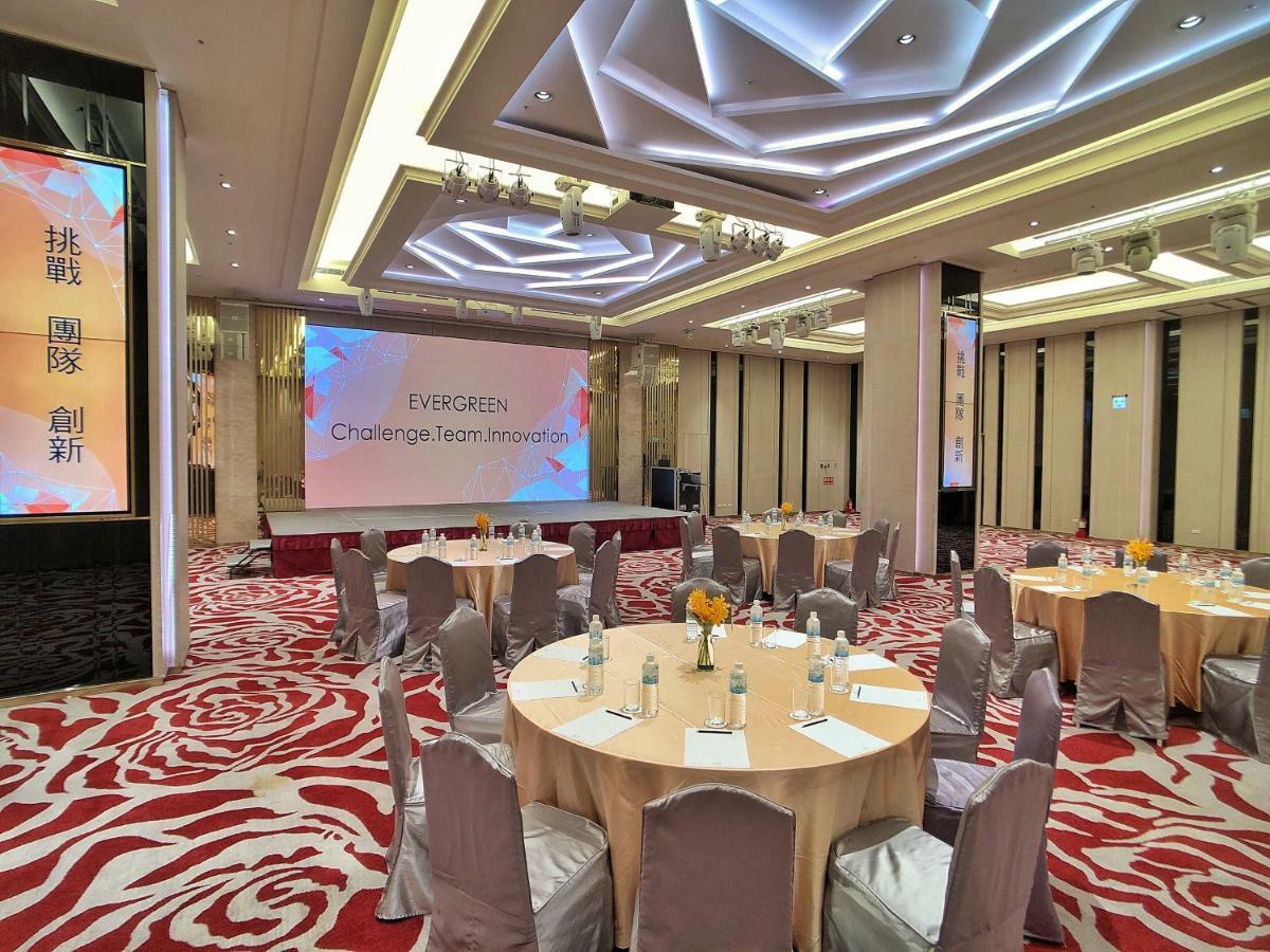 Evergreen Laurel Hotel - Taichung Bagian luar foto The photo shows a conference or event space set up for a gathering. The room features several round tables with light-colored tablecloths and chairs, each with decoration, possibly for dining or discussion. A large screen displays the text "EVERGREEN